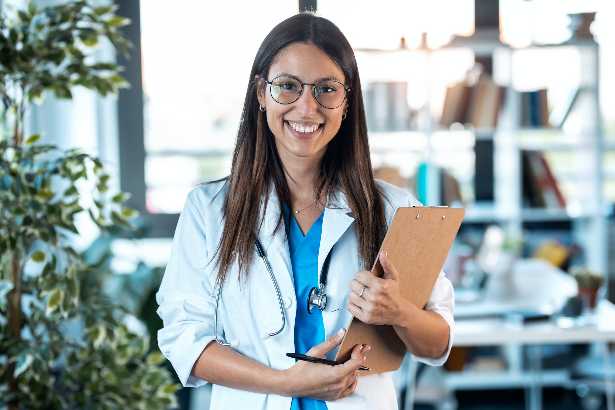 happy young female doctor smiling and looking at camera while holding a clipboard